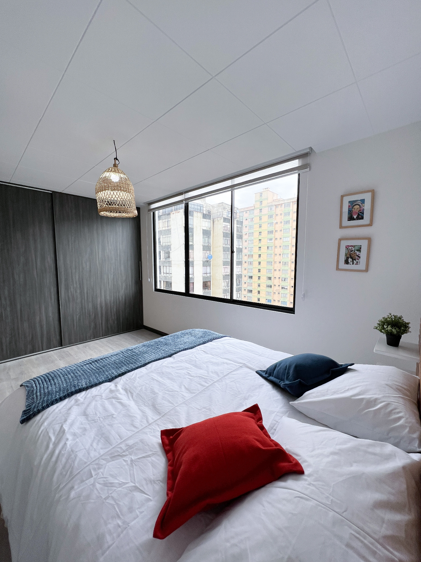 Light-filled bedroom at Calm Illimani 2 with crisp white bedding, woven lamp, and red and navy cushions