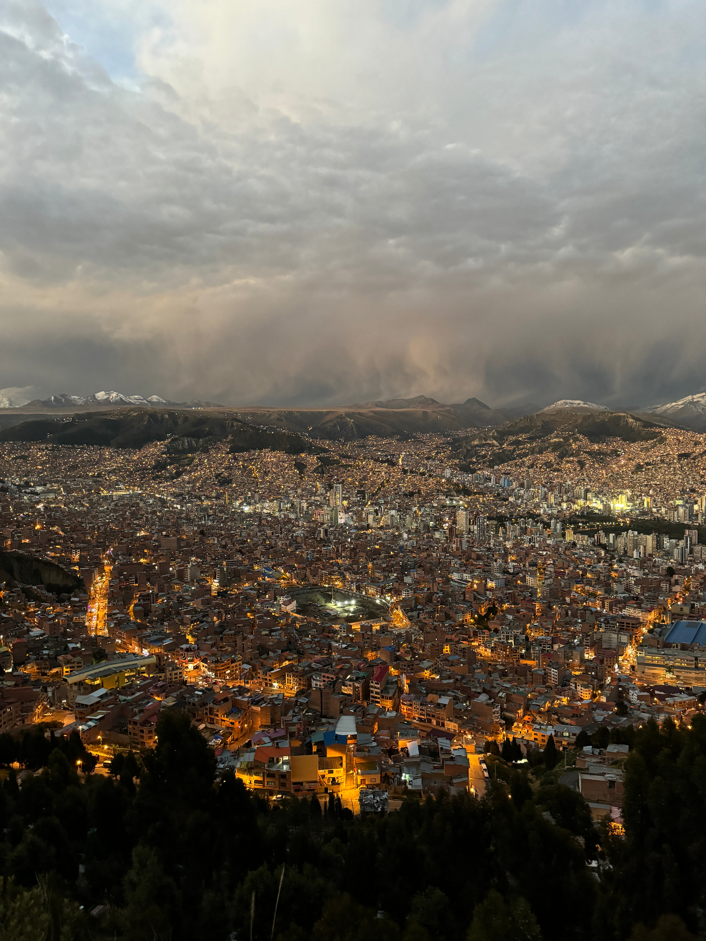 La Paz at nightfall, city lights glowing under a dramatic cloudy sky